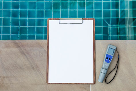 Blank white paper on clipboard on the side of inground pool next to a digital water tester