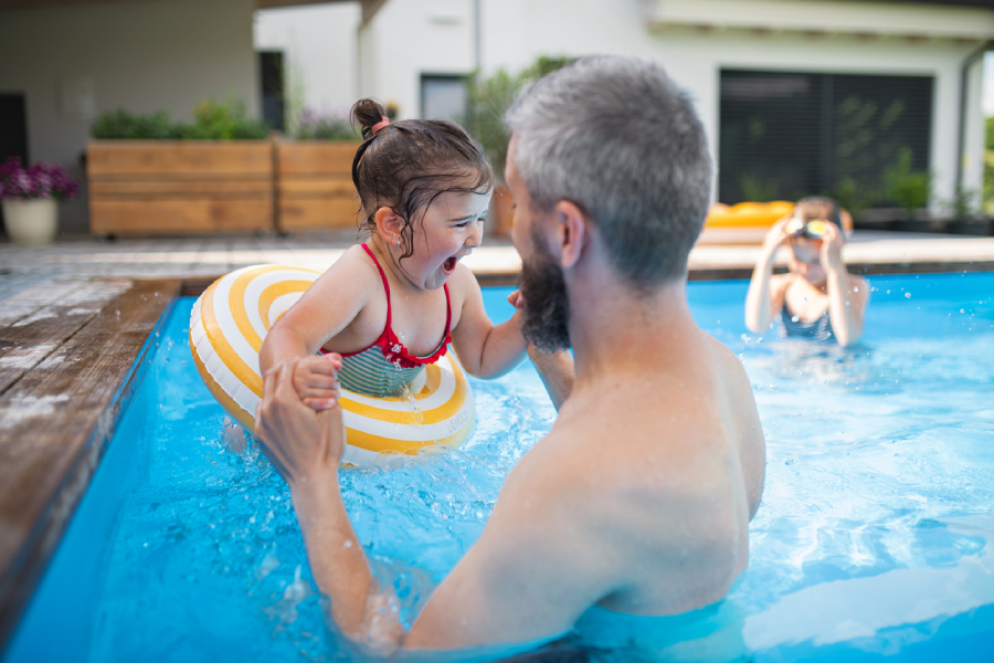 Family members play in backyard pool on sunny day