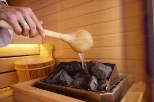 Person pouring water on hot stones in sauna